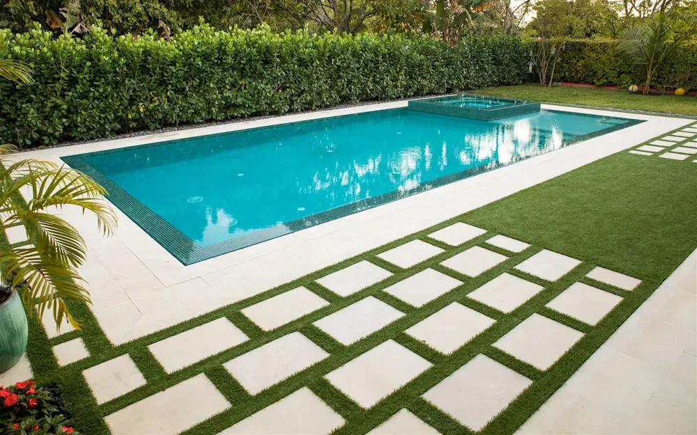 Rectangular pool with spa surrounded by large stone pavers set in artificial turf and lush green hedges