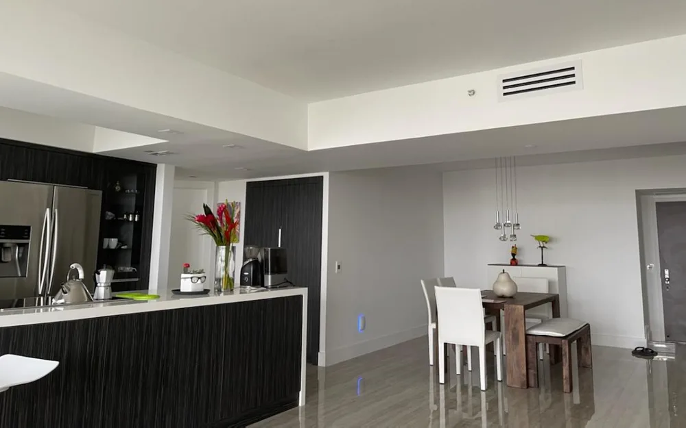 Modern open-plan kitchen and dining area with a white linear slot diffuser installed flush in the ceiling