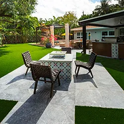 Outdoor patio with a square fire table, wicker chairs, and artificial turf beside a pergola and pool