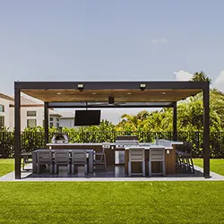 Dark aluminum louvered pergola with outdoor kitchen bar, bar stools, grill, and TV over lush lawn