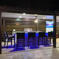 Outdoor bar area with blue LED lighting under countertop, bar stools, and mounted screens at night
