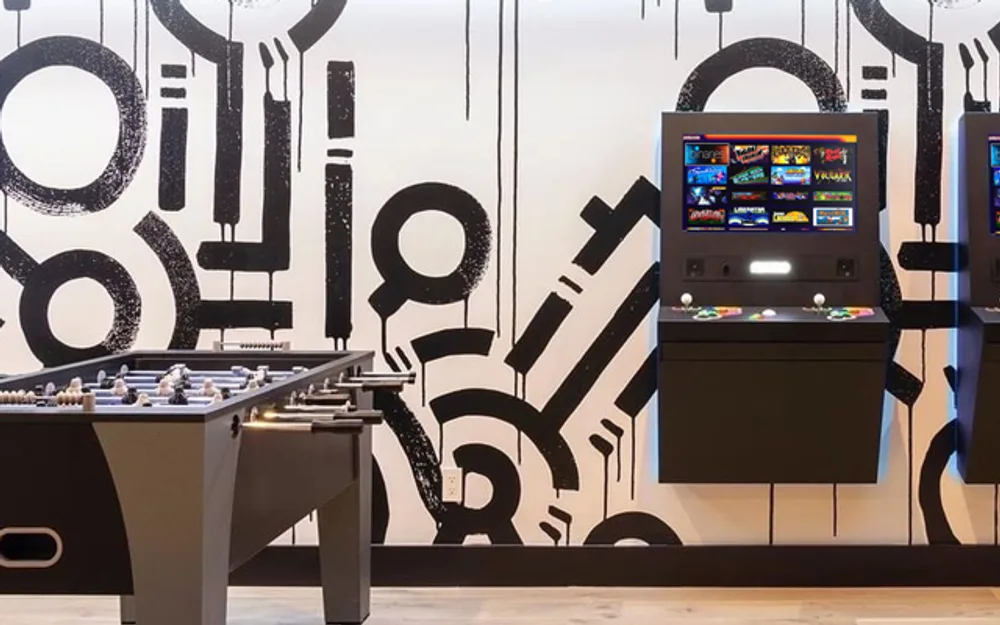Game room with two Polycade arcade cabinets and a foosball table against a bold black-and-white mural wall