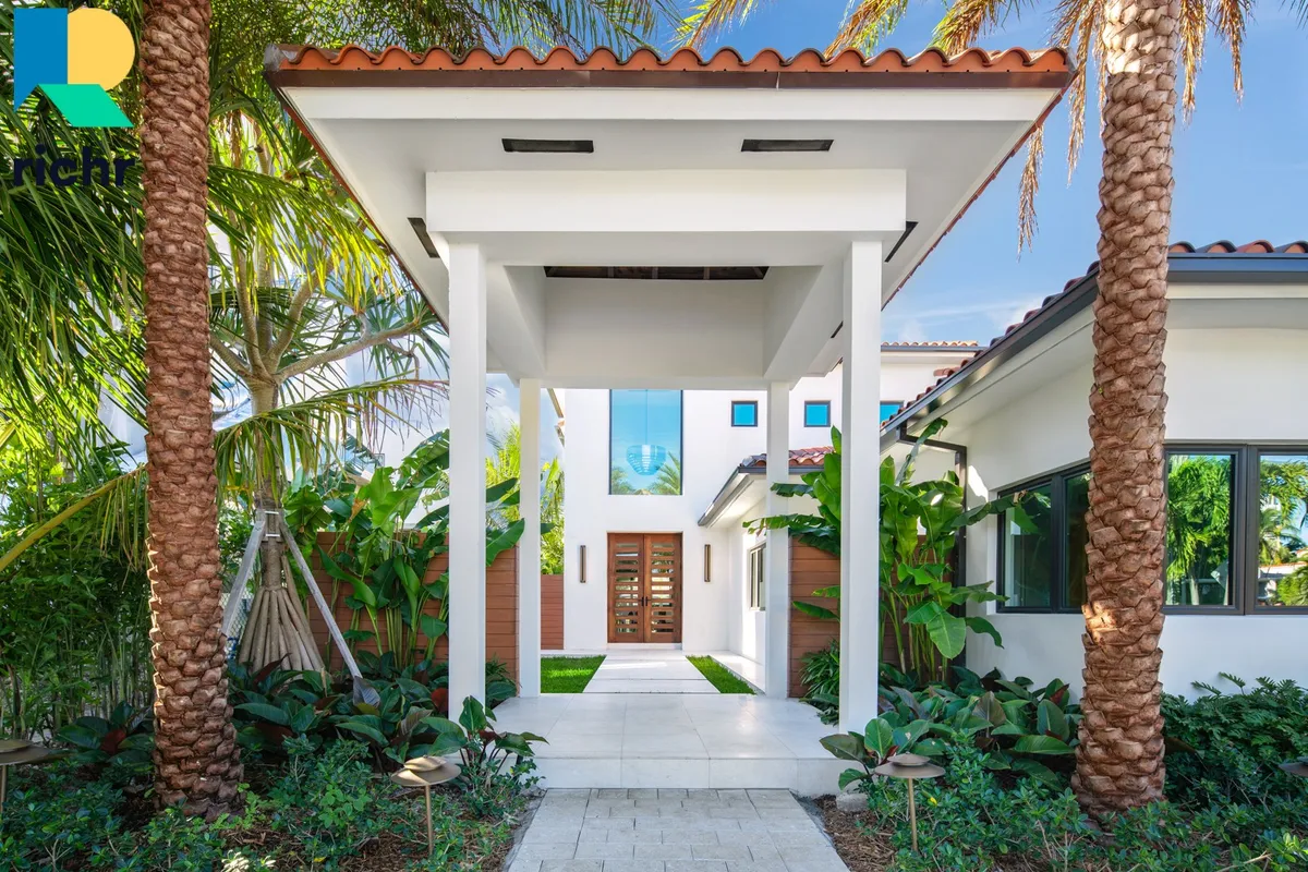 Gated entry walkway of a white Mediterranean estate flanked by palm trees, Richr logo overlay