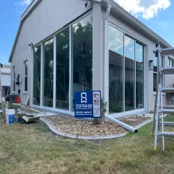 Floor-to-ceiling impact windows being installed on a modern white home exterior with Statewide signage