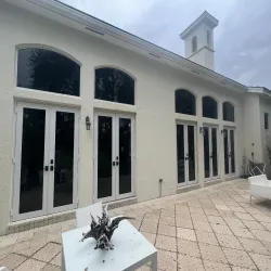 Elegant white home facade with arched French doors and transom windows on a stone patio