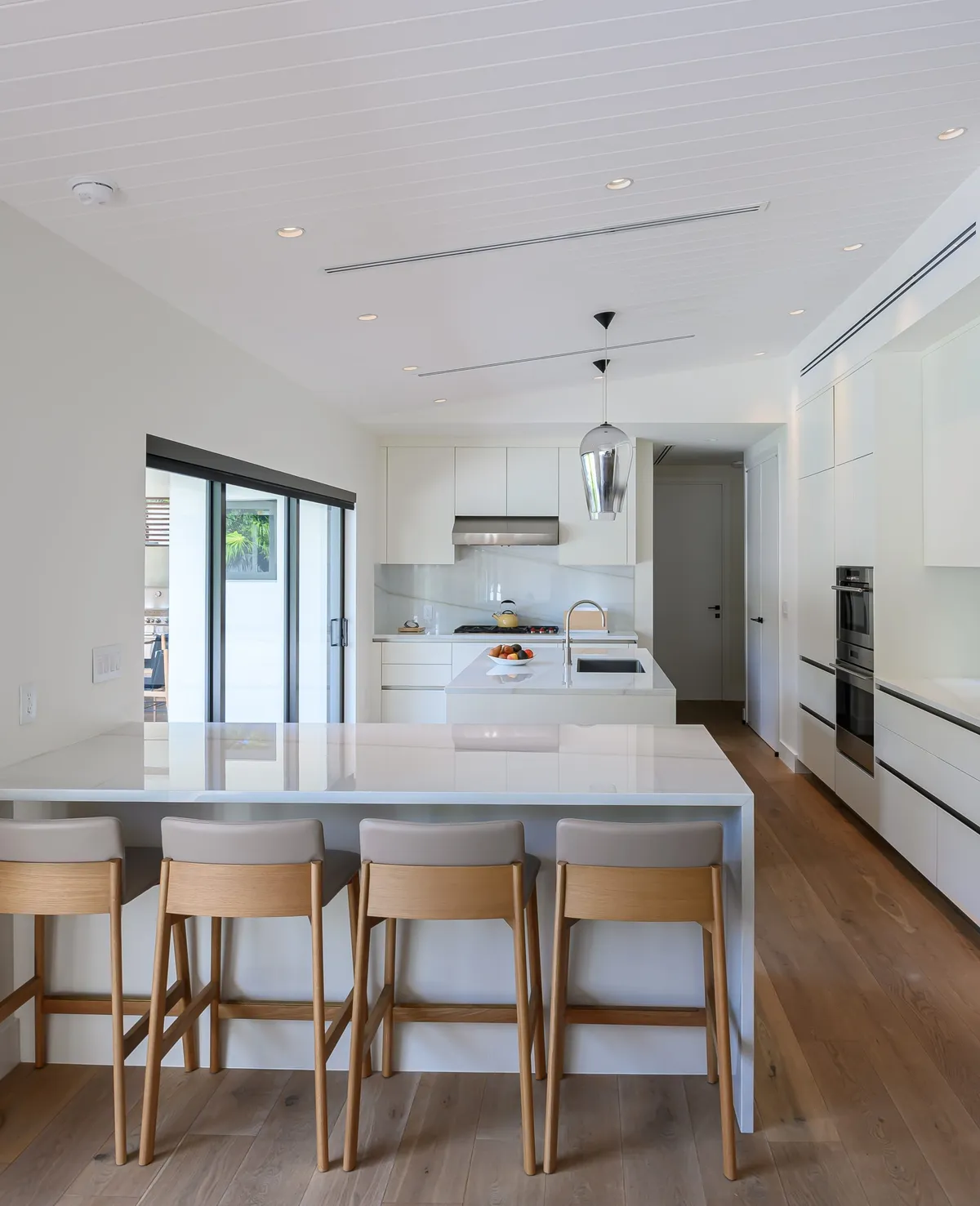 Bright white modern kitchen with large island, bar stools, and floor-to-ceiling cabinets
