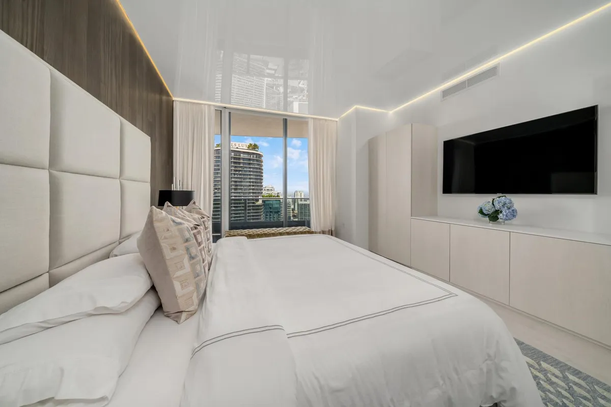 Luxury high-rise bedroom with tufted headboard, glossy stretch ceiling, and city skyline view