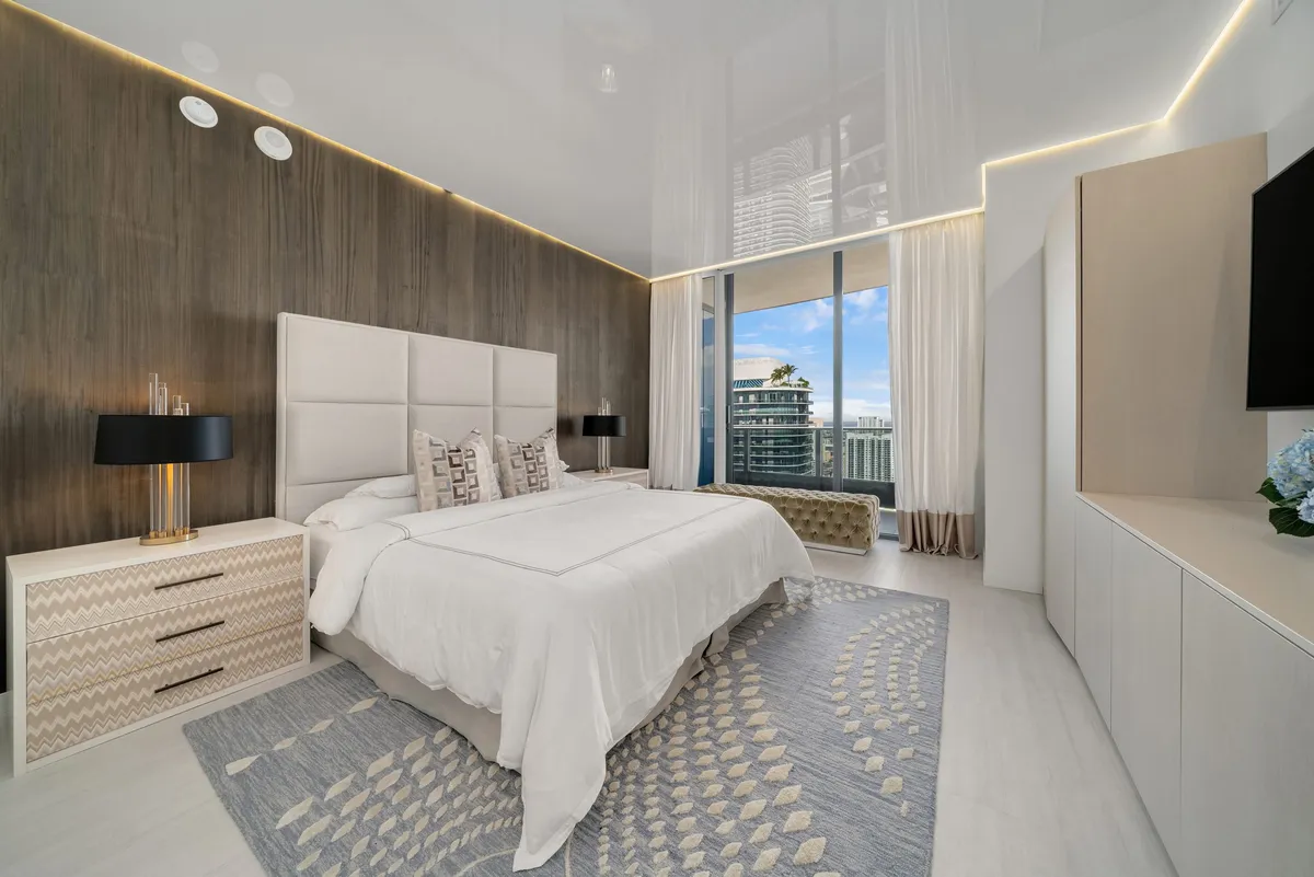 Luxury master bedroom with wood accent wall, tufted headboard, and high-rise city view