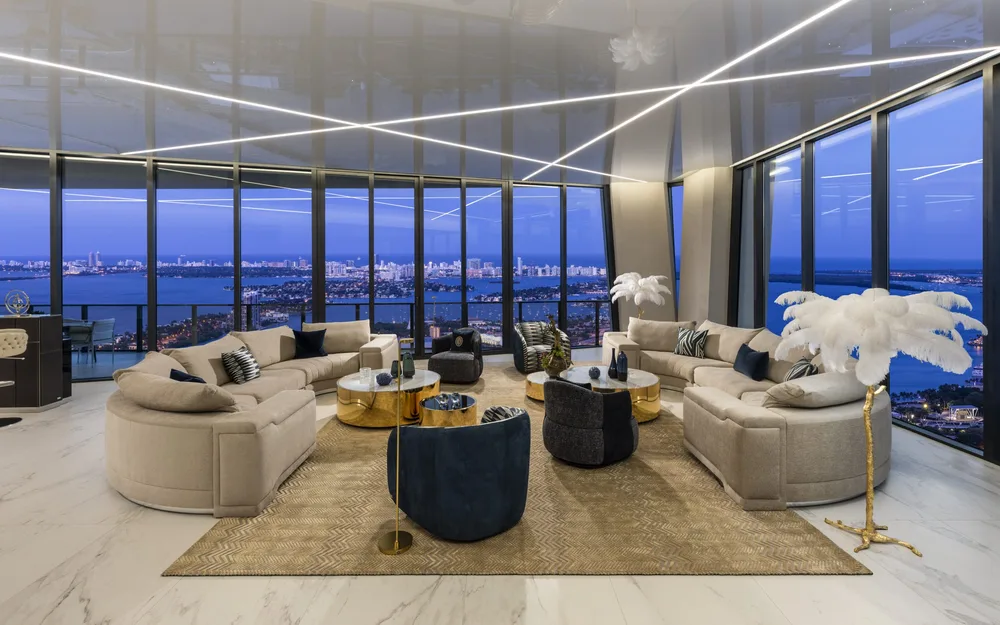 Glamorous nighttime penthouse living room with curved sofas, LED ceiling, and panoramic Miami skyline